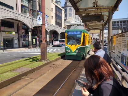#1 tram arrives at the platform in the Tenmonkan shopping district, green strips of grass line the tram lines.