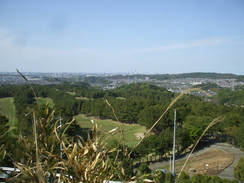 View north over golf course toward tall buildings in Yokohama and Tōkyō from path around Kamakura.