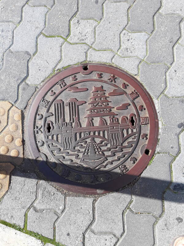 Custom manhole cover in Osaka showing the castle and shipping.