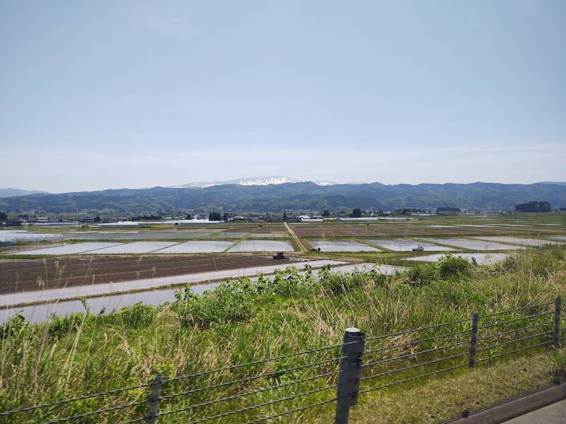 View from the bus from Tsuruoka through nearby agricultural plains: large rice paddies with mountains in the distance.