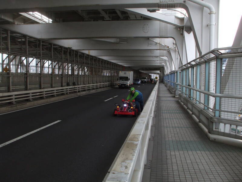 Cosplayer pushing his go-kart Rainbow Bridge over Tokyo Harbor while dressed as Mario.