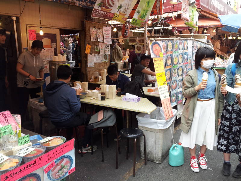 Girl with a face mask prepares to eat soft-serve ice cream at a small restaurant in the Ameya-Yokochō market under the Yamanote Line tracks.