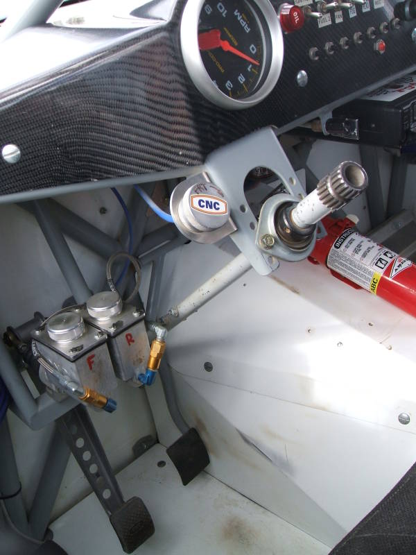 Interior of Baja 1000 off-road race truck: clutch, brake, and accelerator pedals, dashboard and instrument panel, steering column, fire extinguisher.