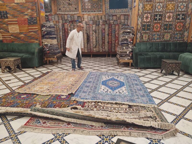 Carpet wallah wrestling a pile of woolen carpets in Fez el Bali medina along Tala'a Sghira.