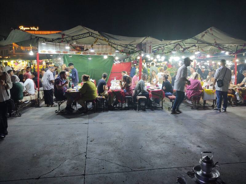 ALT: People eating at food stalls on Sāḥat Jāmi' al-Fanā', or The Mosque at the End of the World, in central Marrakech.