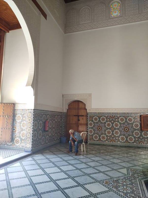 Man in a chair in the entry chamber of the Mausoleum of Moulay Ismail.
