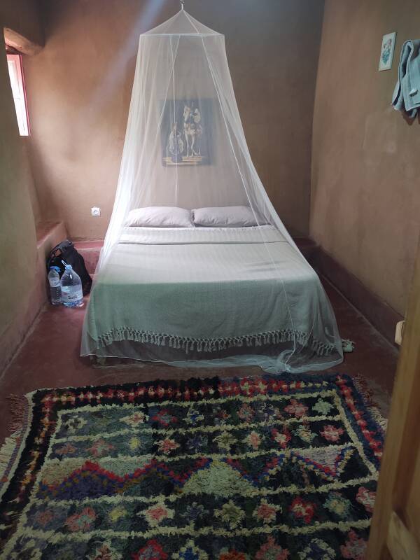 Bed, carpet, and mosquito net in my room at Auberge La Palmeraie.