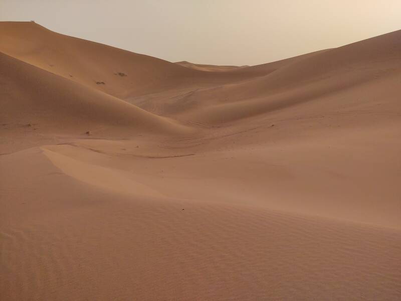 People on top of a 150-meter dune in the distance, off-road vehicle tracks in the foreground.