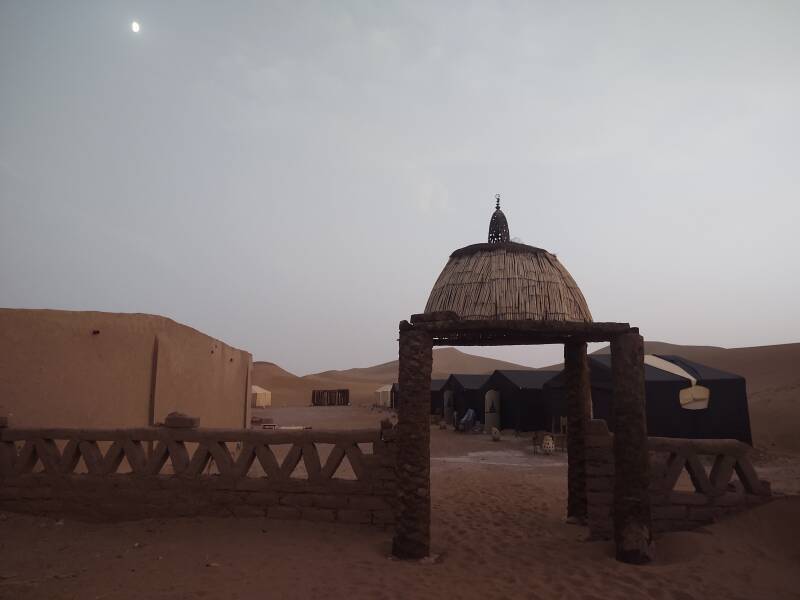 Gateway into the camp at Erg Chigaga, moon above tents and dunes.