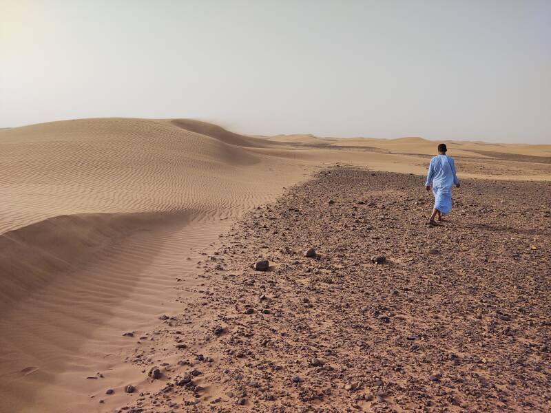 A man in a blue djellaba walks past ripples on small dunes east of Erg Chigaga.