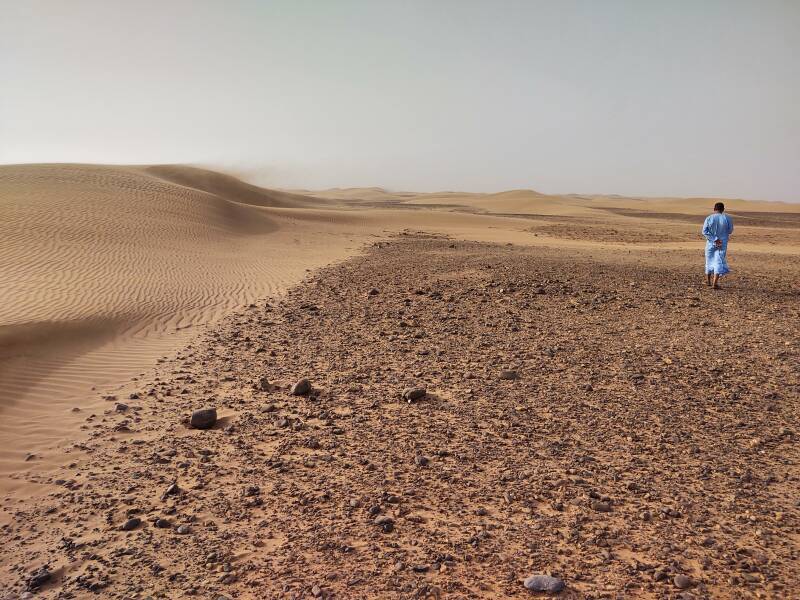 A man in a blue djellaba walks past ripples on small dunes east of Erg Chigaga.