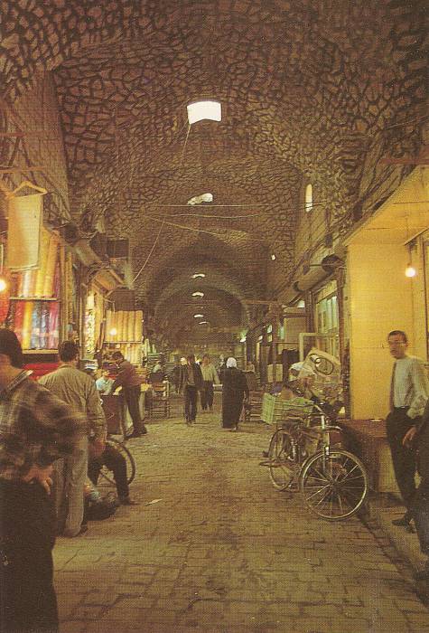 Arched and domed passageway in the bazaars in Aleppo, Syria. Shops and shopkeepers on either side, bicycles, and pedestrians.