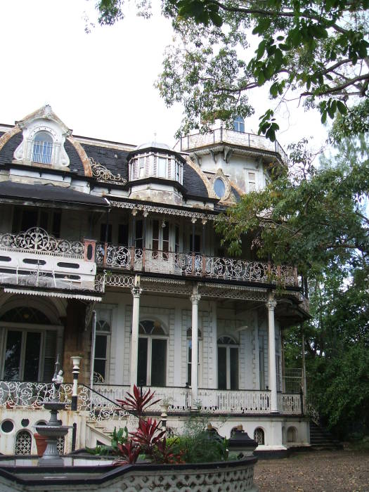 Dilapidated colonial mansion in Trinidad: ornate wood trim, gables and cupolas, tropical trees.