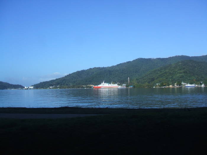 Looking across the Gulf of Paria: The red and white ferry to Venezuela, the green lushly forested hills, and some buildings of Chaguaramas Town.
