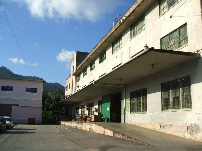 A simple three-story industrial building: a loading dock and some windows.  The mountainous jungle is beyond.