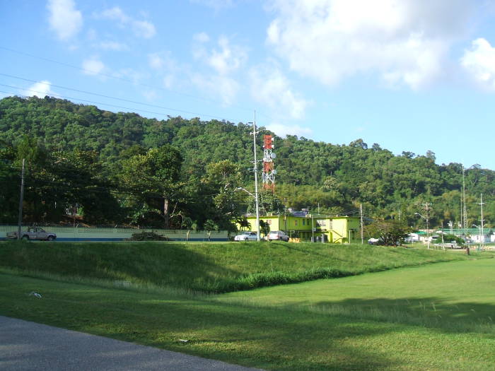 A microwave radio tower, some brightly painted buildings, and a jungle covered hill.