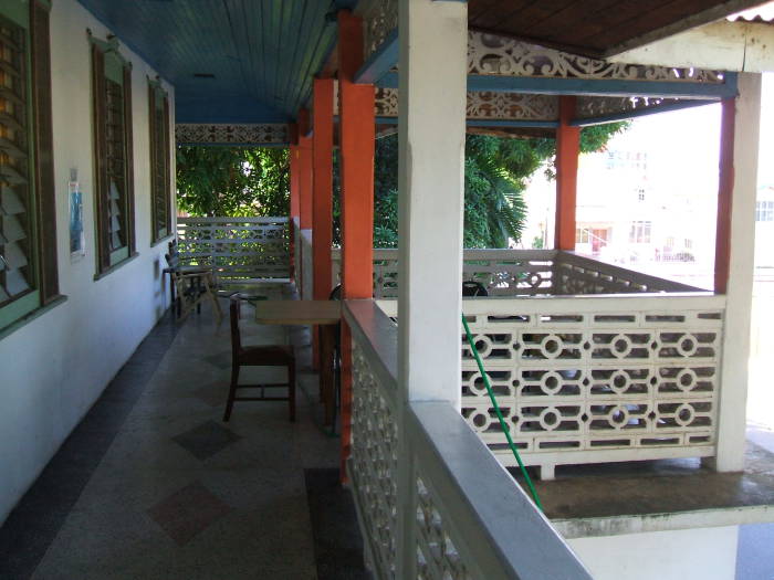 A shaded balcony with some tables and chairs, overlooking the street and the park at Pearl's Guesthouse in Trinidad.