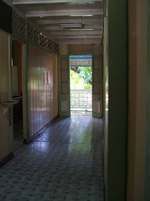 A hallway with linoleum floor and cheerily painted walls opening onto a balcony at Pearl's Guesthouse in Trinidad.