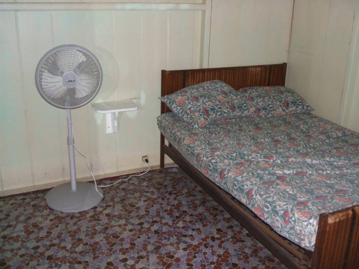 A double bed and an electric fan in a guest room at Pearl's Guesthouse in Trinidad.