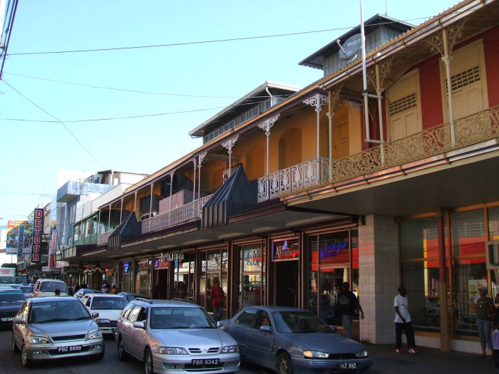 Traffic and shops in downtown Port-of-Spain, Trinidad, with balconies above the shops.