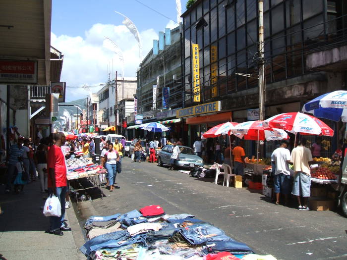 Downtown Port-of-Spain, Trinidad. Shopping centers indoors, and markets along the sidewalk and extending into the street.