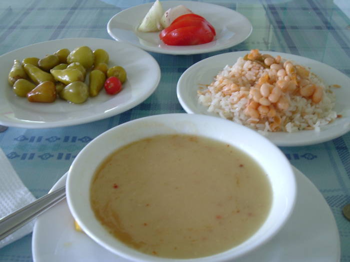 Turkish meal of lentil soup, plav, and pepper, tomato and onion garnish.