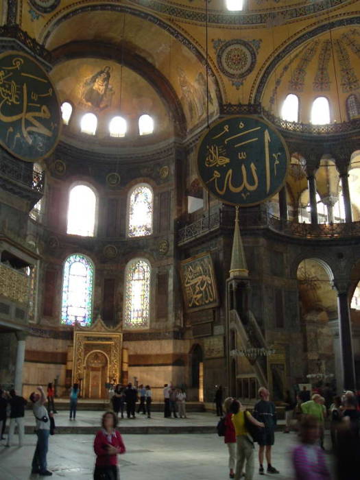 Interior of the Hagia Sophia or Aya Sofya, in Istanbul.  Mosaic of the Virgin Mary and Jesus in a large semi-dome over the altar area.  Mihrab showing the direction to Mecca.  Minbar or pulpit from which the Imam delivers the sermon.  Large medallions with Koranic quotes in large calligraphy.
