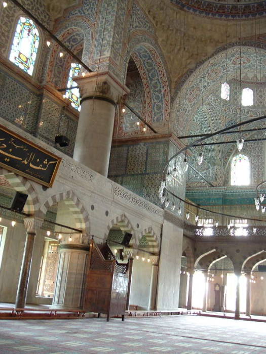 Interior of the Blue mosque or Sultanahmet Cami, in Istanbul.  Mihrab and Minbar.  Large chandeliers above many prayer rugs.