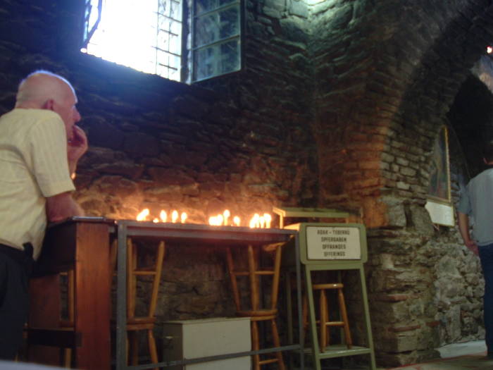 Prayer inside the Virgin Mary's house at Maryemana Evi.  A row of candles.  Stone walls.