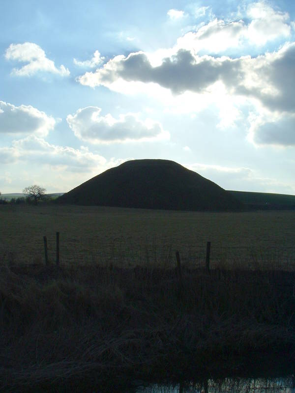 Silbury Hill is silhouetted before the sun.
