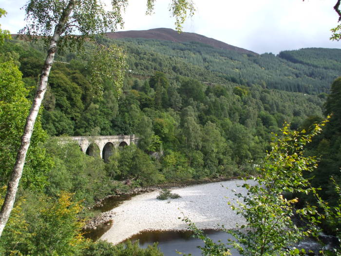 Arched railroad viaduct along a river in Scotland.
