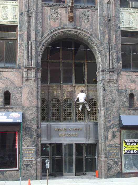 Man cleaning brass entryway on David Stott Building in downtown Detroit.