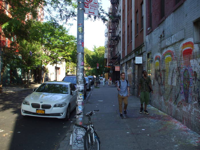 Two hipster dudes walking down a sidewalk past colorful graffiti on the Lower East Side.
