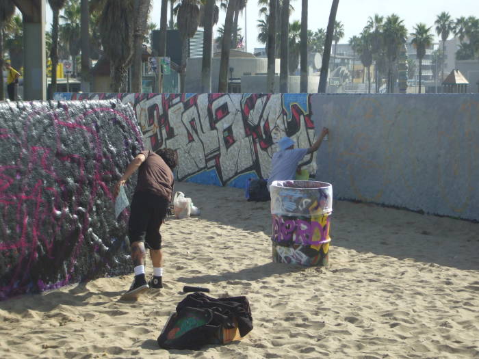 Two artists painting graffiti on the beach in Venice, California.