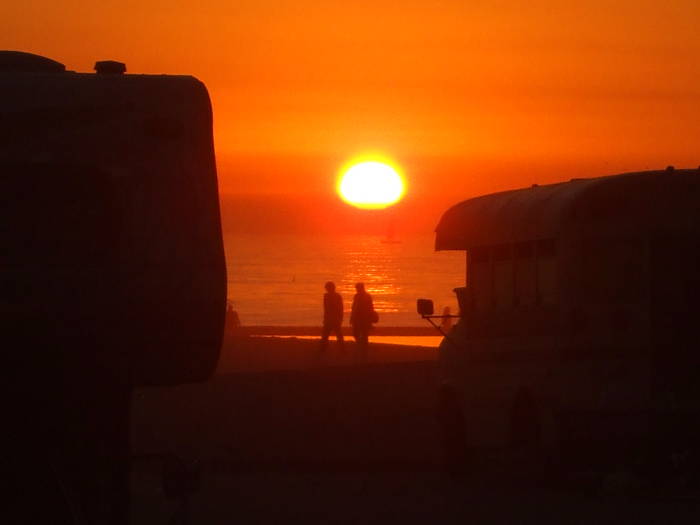 Sunset over Venice Beach and the Pacific Ocean.  People, a camper, and a bus.